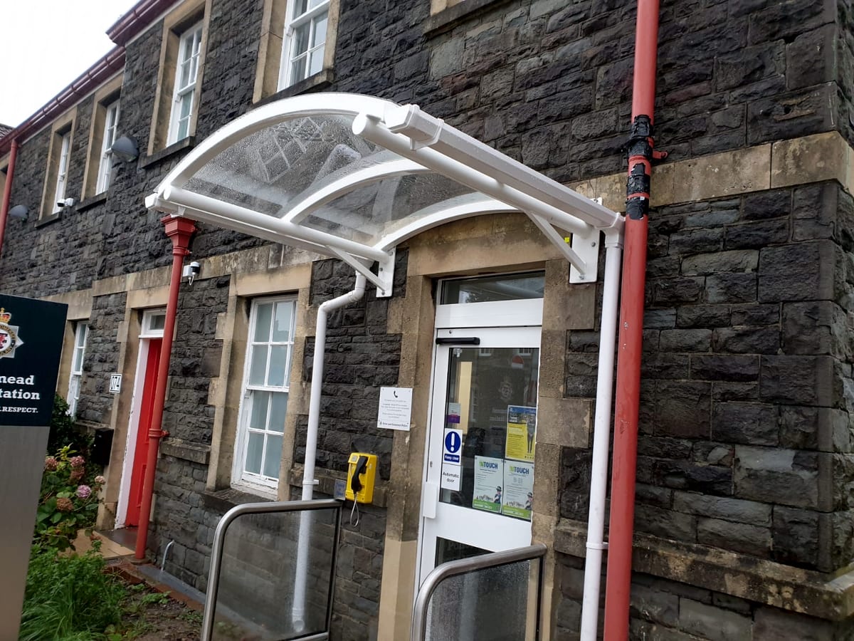 Small curved entrance canopy in white powder-coated steel over a doorway