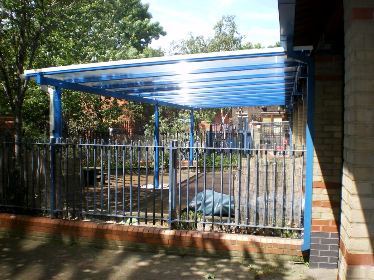 Arched entrance canopy in blue powder-coated steel over a school playground gate